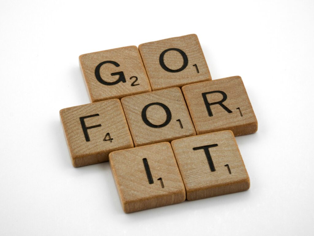 Close-up of Scrabble tiles spelling 'Go for it' on a white background.